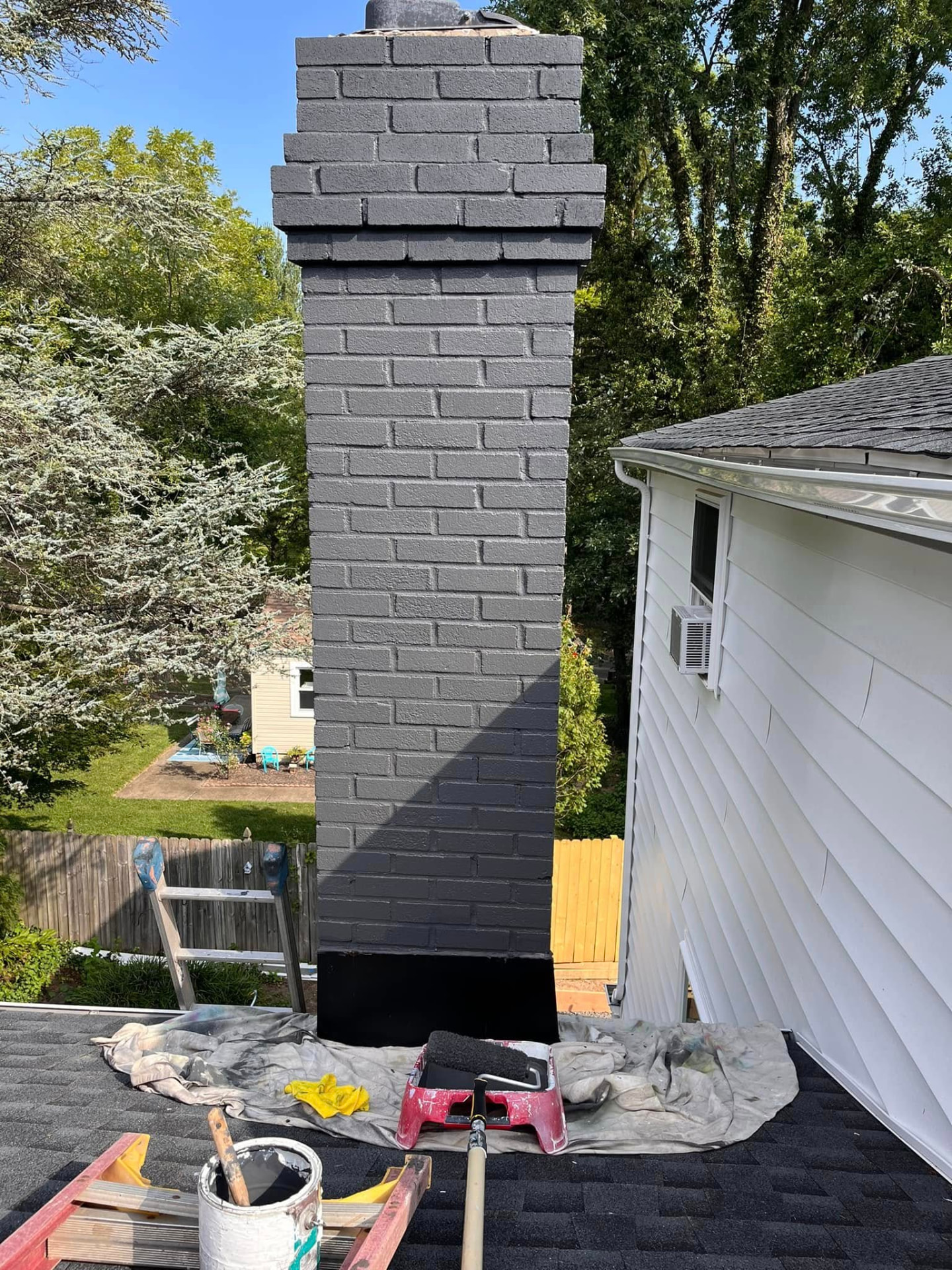 Brick chimney after being refinished in charcoal gray on a white house roof